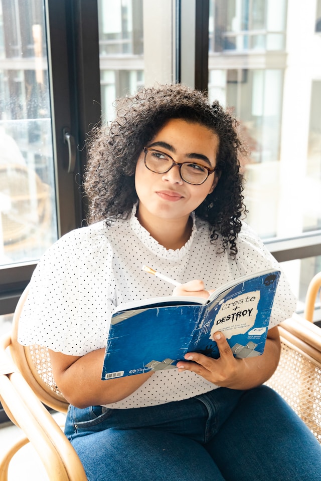 Thoughtful black woman, deeply engrossed in journal thinking, meticulously sketches in her notebook